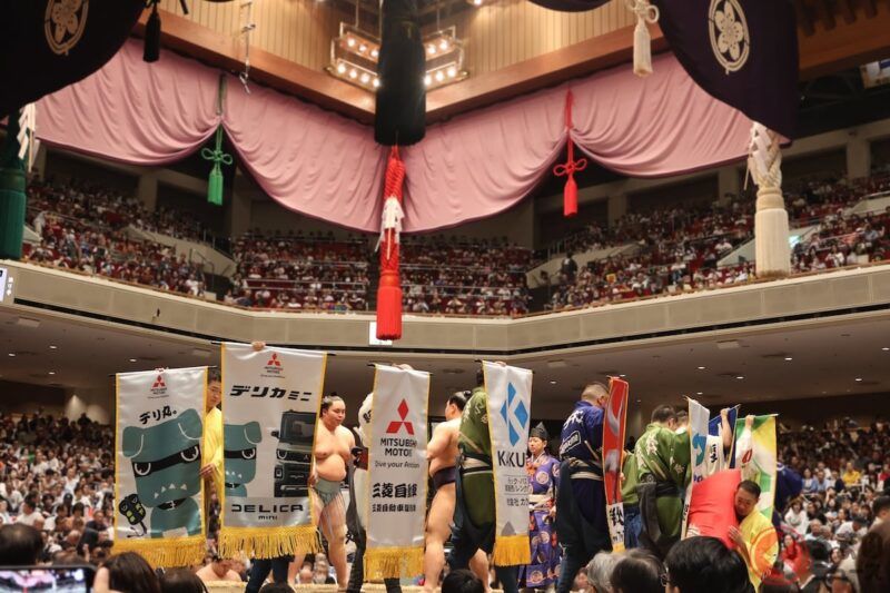 為什麼三菱會在大相撲比賽中提供「懸賞金」？土俵上出現「デリ丸。」的原因是什麼？懸賞旗中所寄託的心意又是什麼？